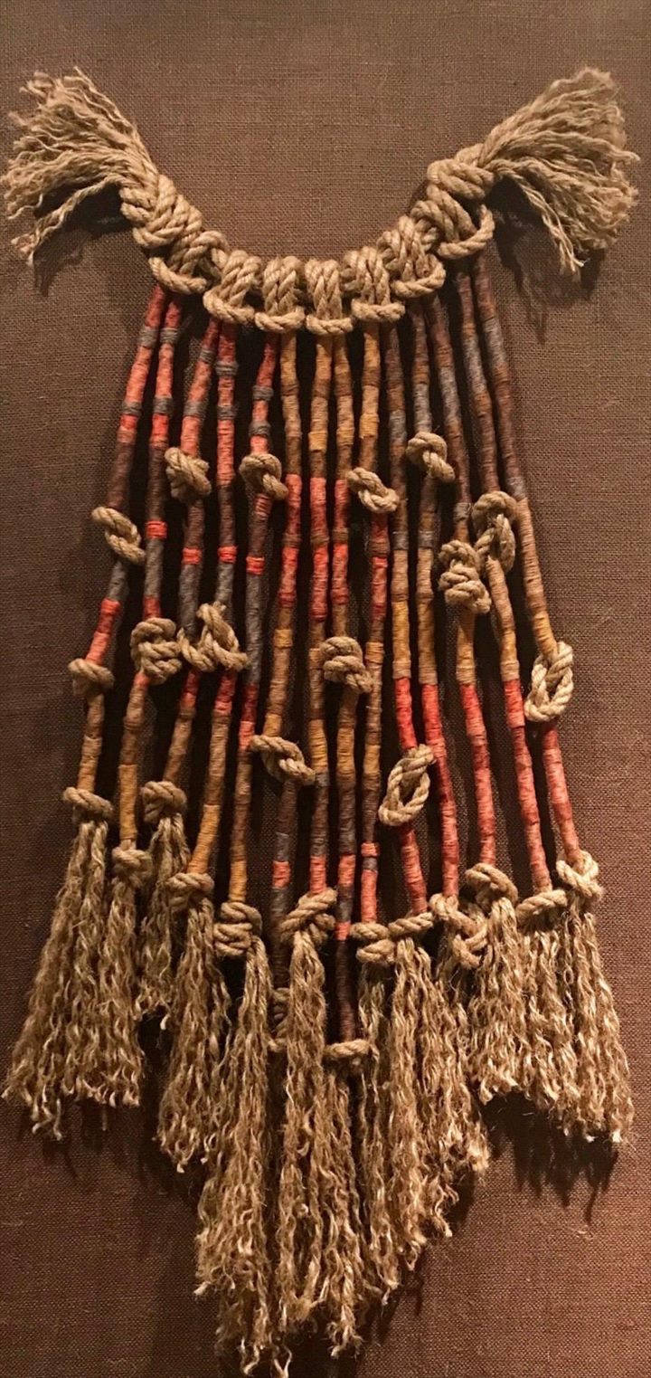 Quipu de cordones gruesos envueltos en fibra roja, ocre y parda, anudados y rematados en flecos, sobre fondo de tela marrón.