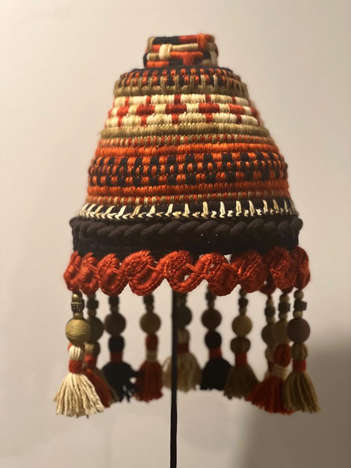 Tocado en forma de campana tejido en naranja, negro y crudo, con cuentas de madera y borlas colgantes.