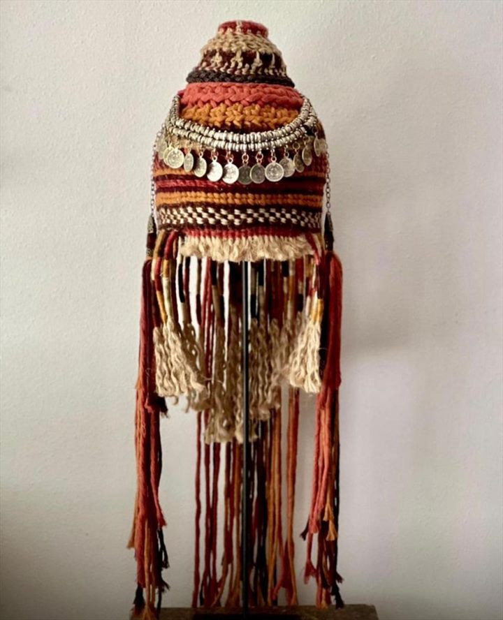 Vestidura ceremonial tejida en rojo, ocre y crudo, con hilera de monedas de plata y largos flecos.